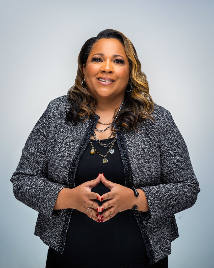 Dr. Latricia Buckner in a charcoal tweed jacket, smiling, hands steepled